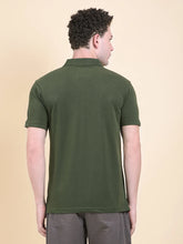 Man wearing a DCYPHR Men's Gravitas Polo - Forest Green against a beige background